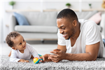 a father or carer on a rug with a baby and some coloured playing blocks